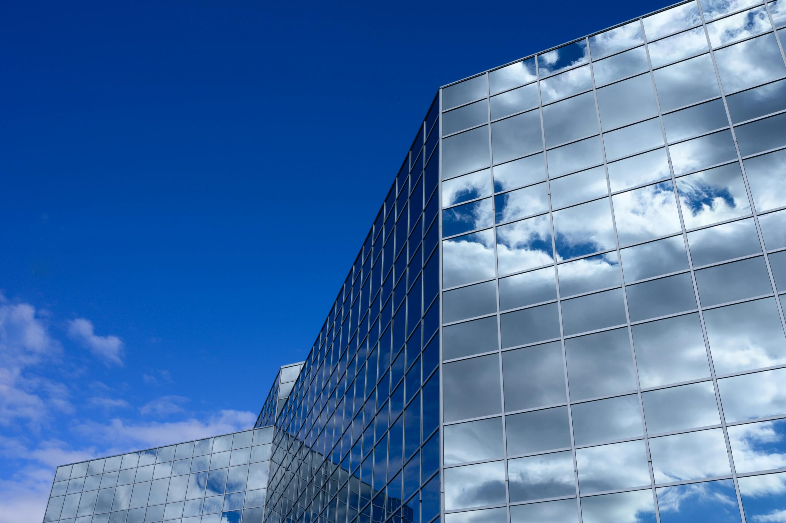 A modern glass skyscraper reflects the blue sky and clouds in an urban setting.